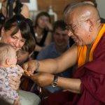 Sherab Gyaltsen Rinpoche ties a blessing string around a very young member of the sangha